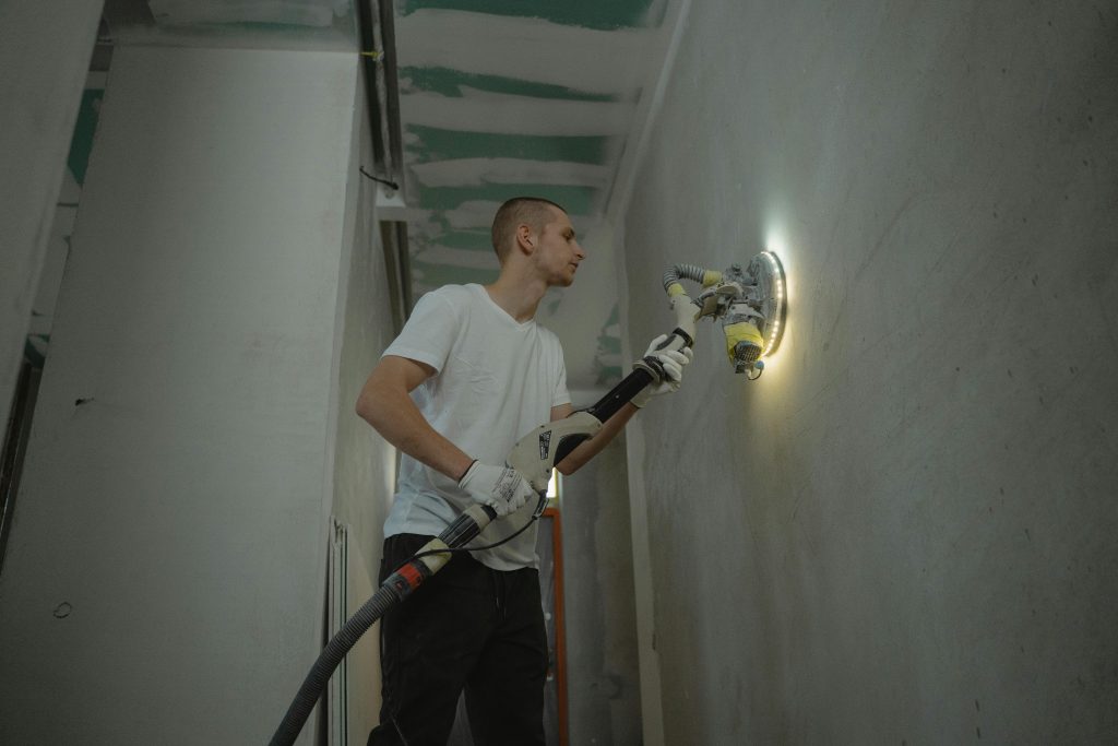 pexels-photo-6473965-6473965 A man sanding an interior wall with an automatic sanding tool during renovation work indoors.